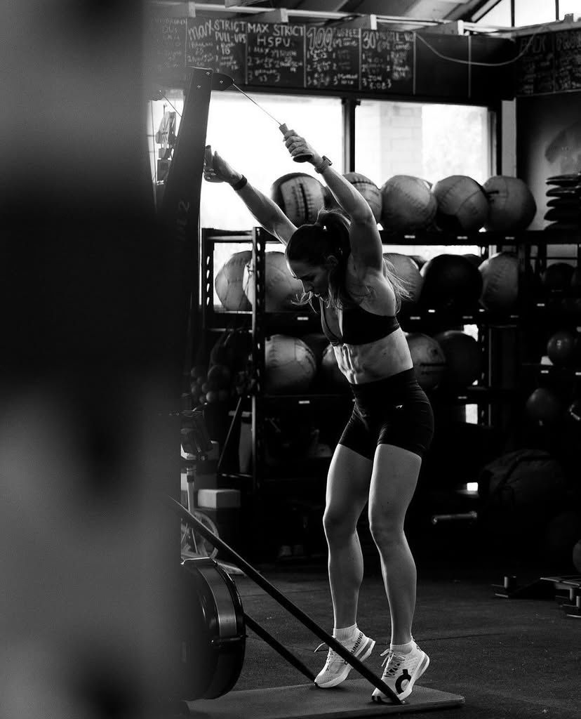 Black and white photo of a woman pulling a cable machine handle overhead in a gym